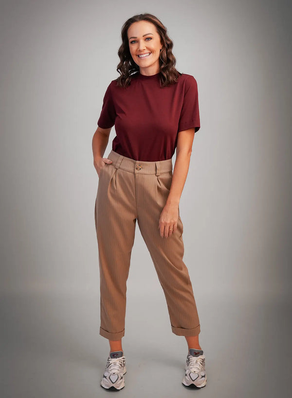 Modelo vestindo calça risca de giz na cor bege, tênis brancos e camisa básica vermelho vinho.