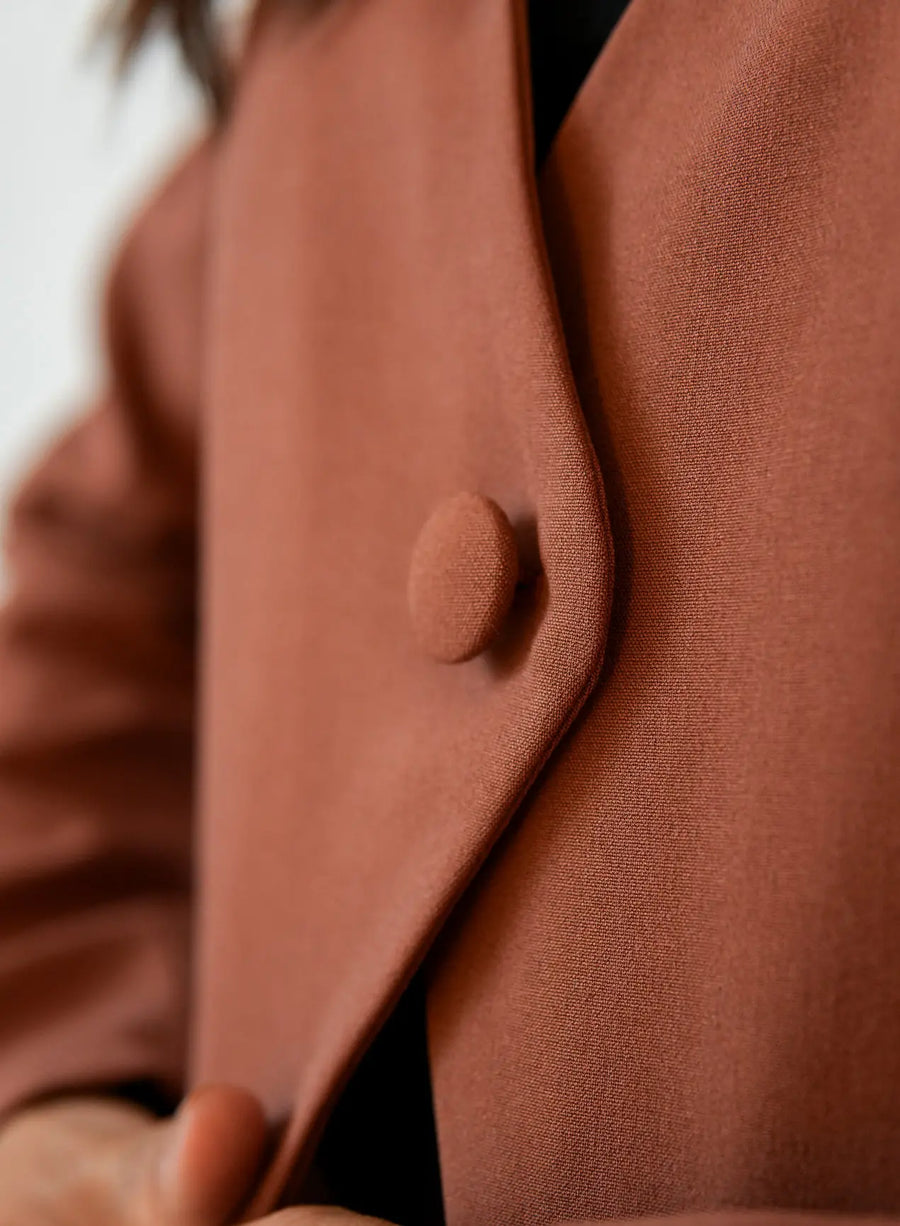 Detalhe de blazer marrom com botão forrado e tecido texturizado.