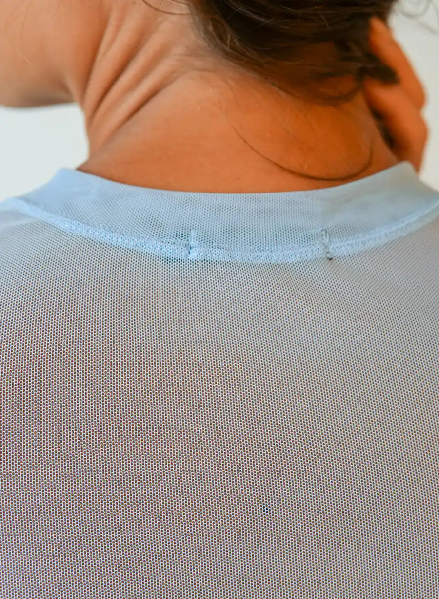 Mulher de costas vestindo Blusa Manga Longa Tule Elisa azul, em frente a fundo neutro, elegante e moderna.