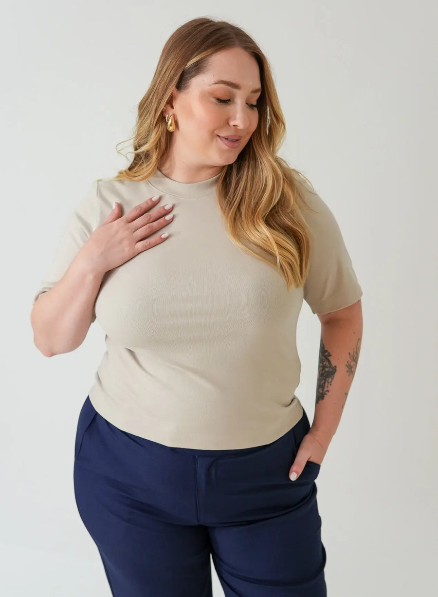 Modelo vestindo blusa tshirt bege e calça azul marinho em fundo neutro.