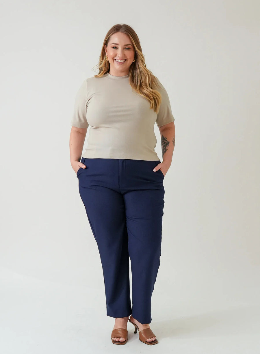 Mulher em pé veste blusa tshirt bege de manga curta e calça azul marinho.