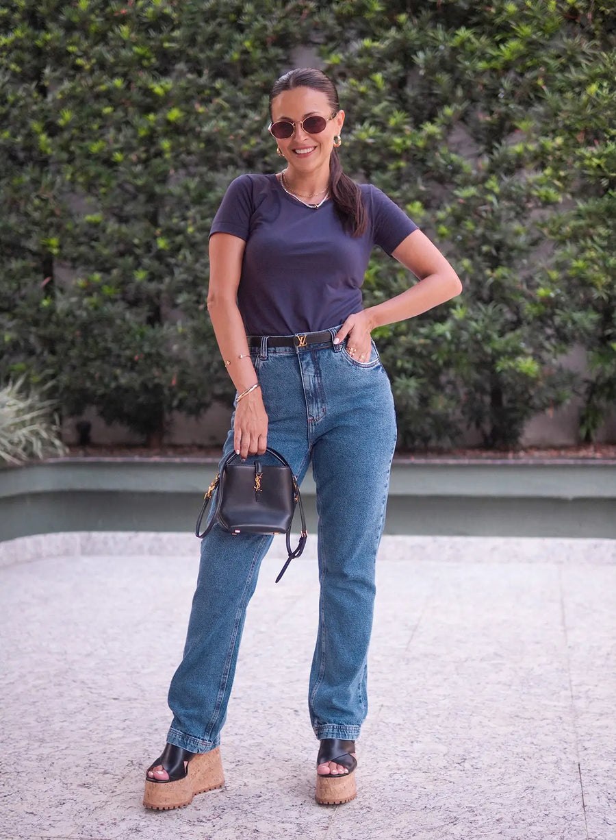 Mulher posando ao ar livre vestindo calça jeans azul e segurando bolsa de mão preta.