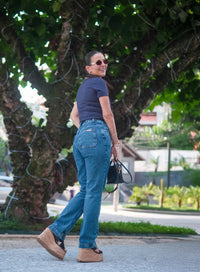 Mulher ao ar livre posa com calça jeans azul, bolsa preta e tamanco.