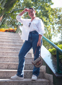 Mulher em escada ao ar livre vestindo calça jeans azul, tênis branco e camisa social branca.