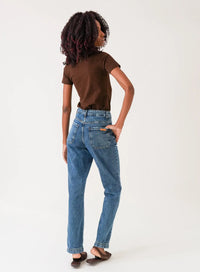 Mulher de costas vestindo calça jeans azul em fundo neutro.