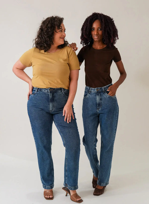 Mulheres posando em fundo neutro vestindo calça jeans azul e blusas básicas.