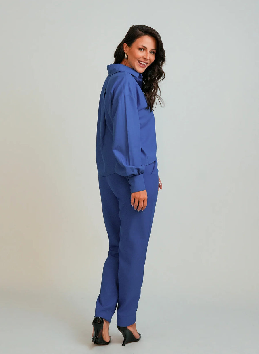 Modelo em fundo neutro vestindo camisa azul feminina e calça azul. Ambas as peças da Elaz.