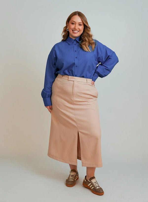 Modelo vestindo camisa azul feminina, saia midi bege e par de tênis marrom.