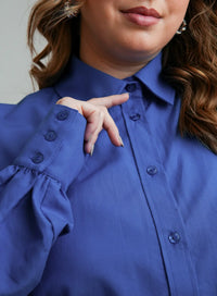 Detalhe da barra da manga da camisa feminina azul, com botões da mesma cor.