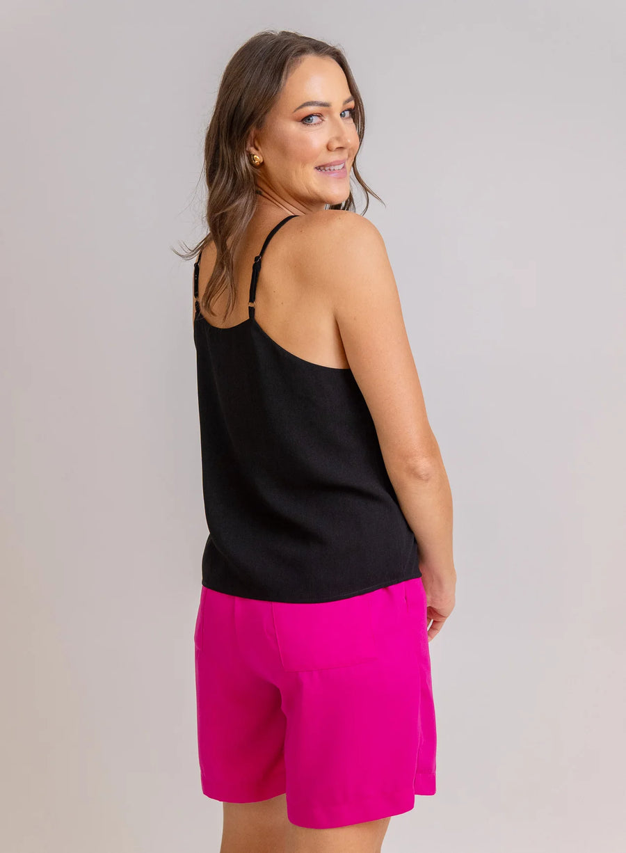 Modelo usando regata preta e shorts rosa vibrante, com acessórios dourados, em fundo neutro.