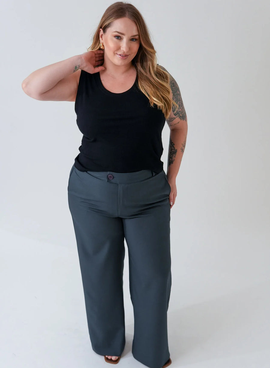Mulher usando regata preta e calça alfaiataria. A modelo combina as peças com acessórios dourados.