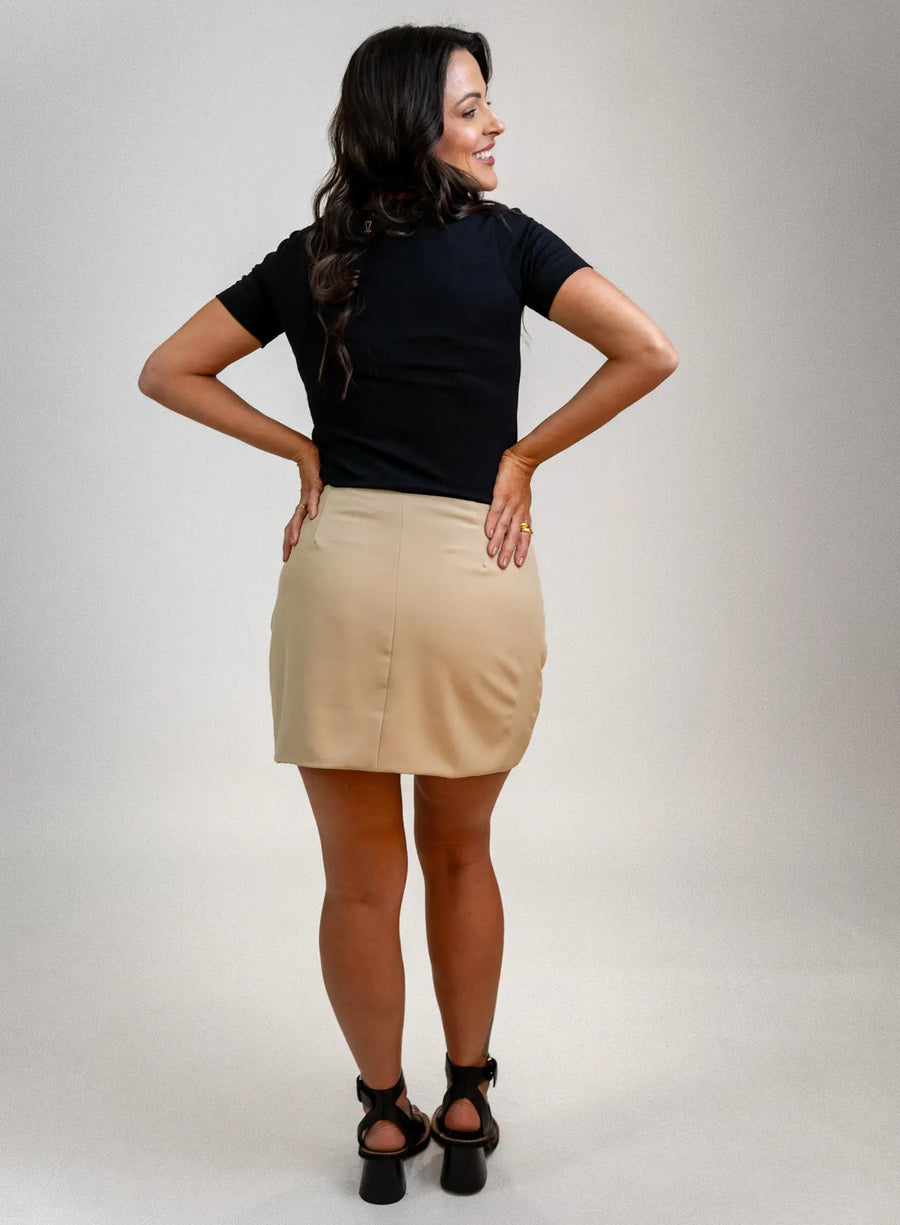 Modelo de costas vestindo saia bege, salto preto e blusa preta.
