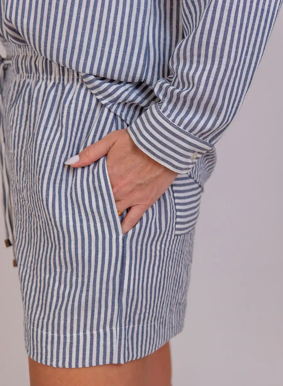 Modelo com mãos no bolso de Short Alfaiataria Azul Laila, alfaiataria azul, cintura alta, peça moderna para compor diferentes looks.